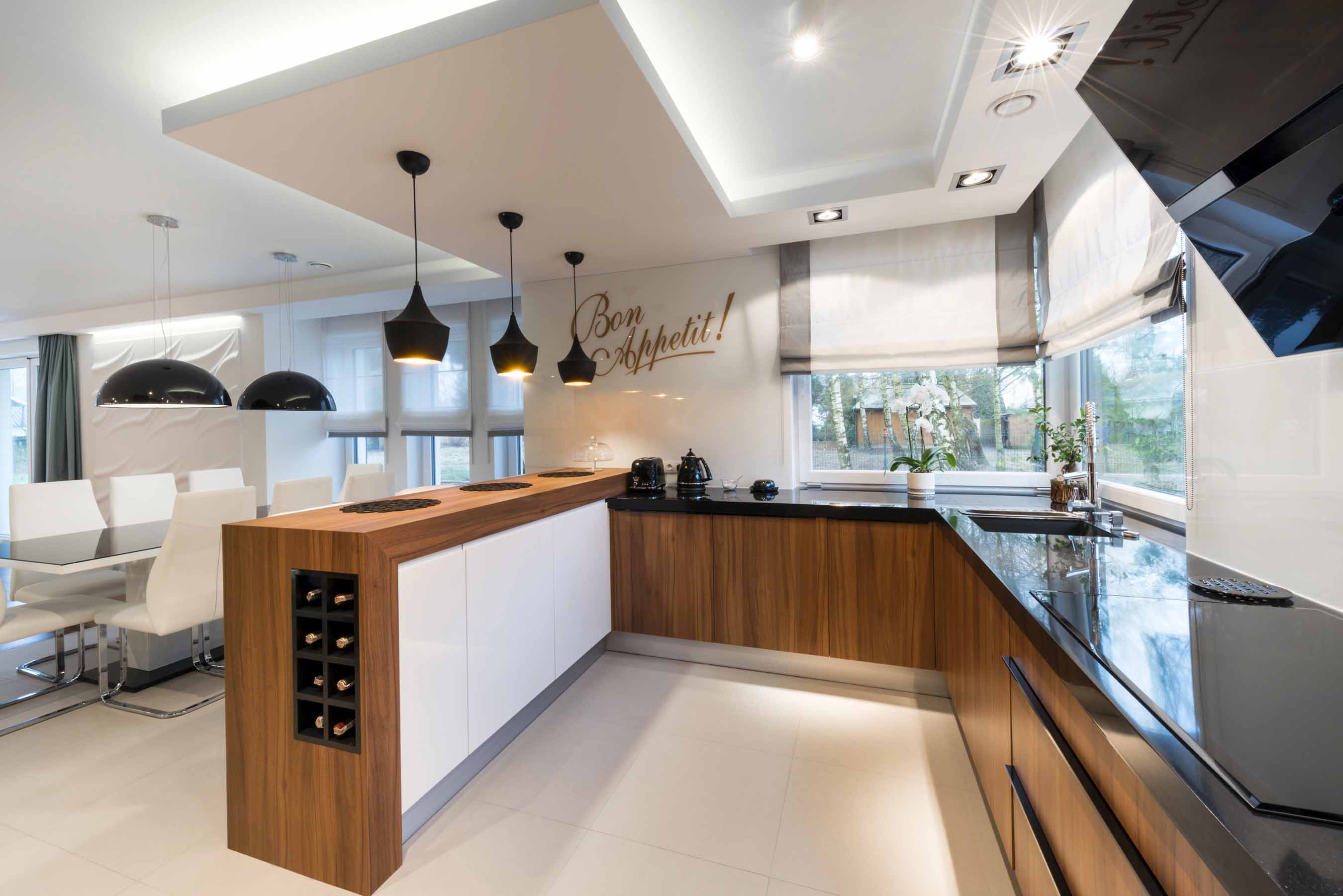 Cuisine contemporaine avec façades en bois, murs blancs, plans de travail noirs et éclairage intégré