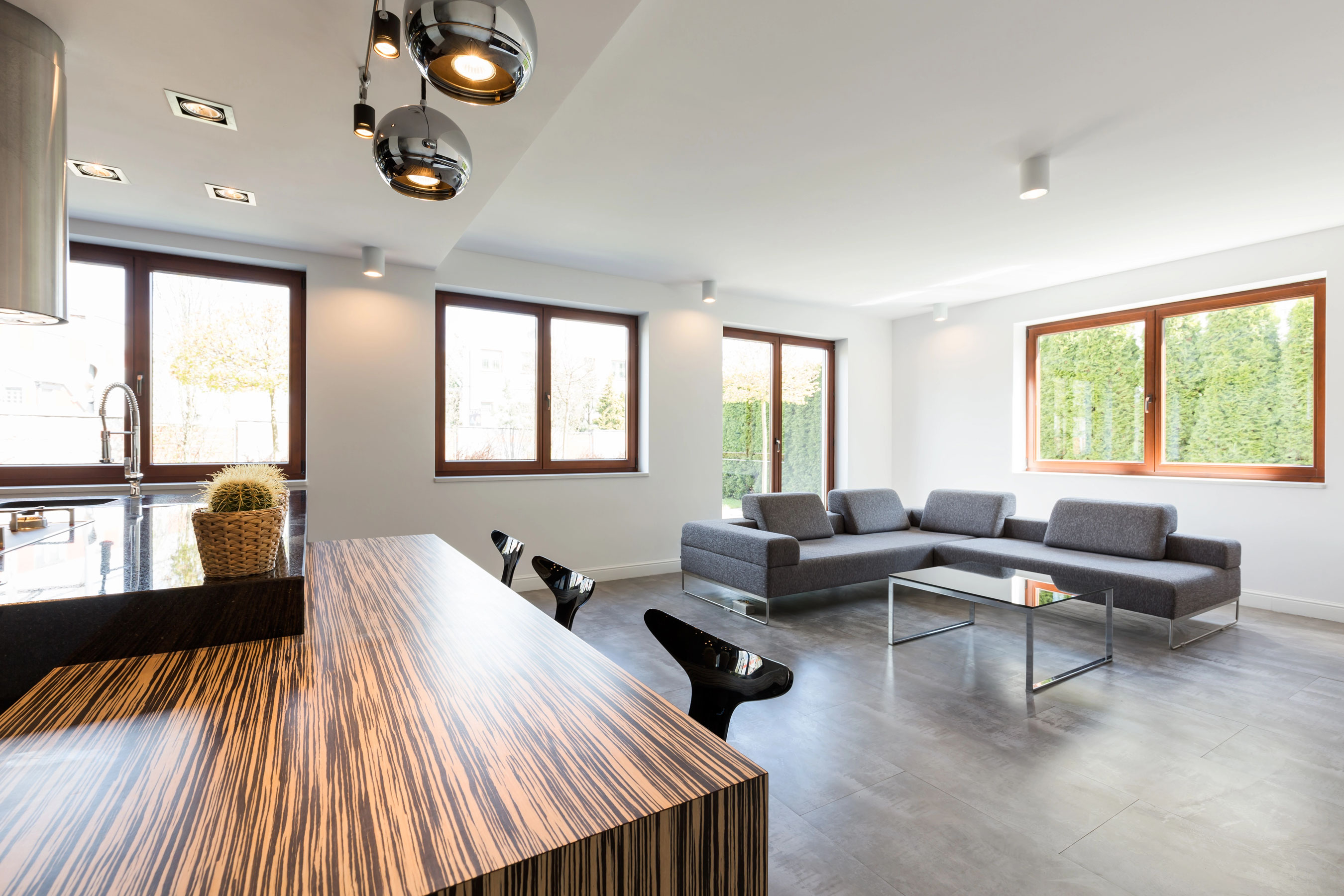Séjour lumineux avec murs blancs, canapé gris, carrelage clair et cuisine ouverte